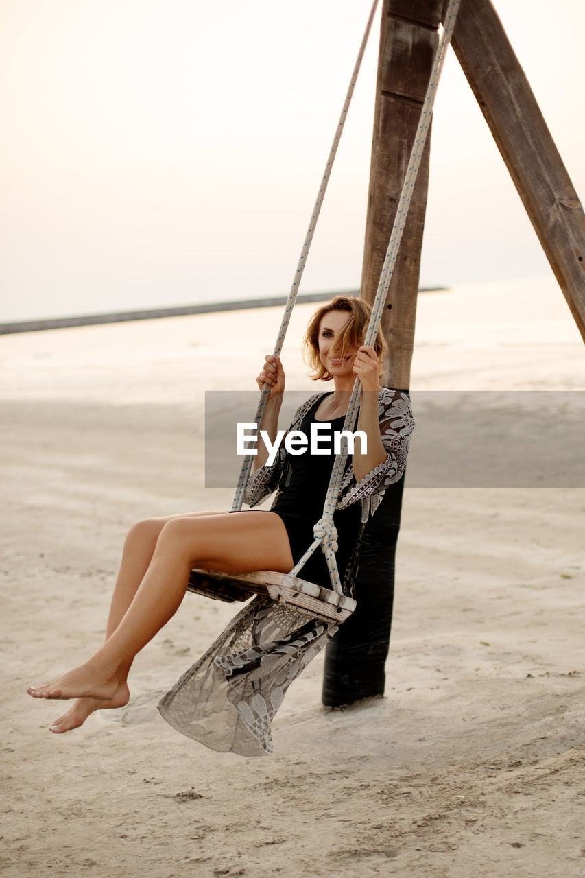 Romantic beautiful woman relaxing on a swing on the beach at sunset, summer vacation, travel