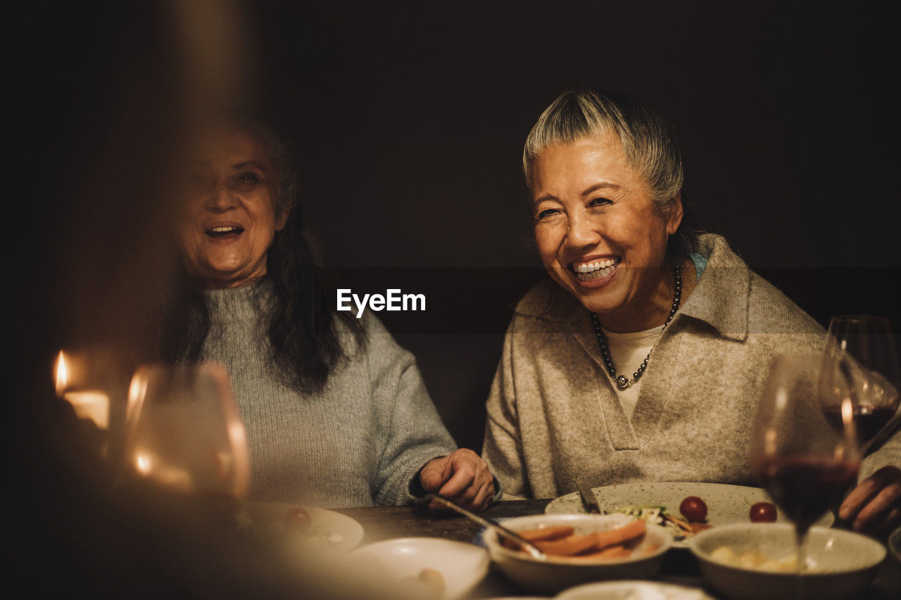 Happy senior woman laughing by female friend at dinner party