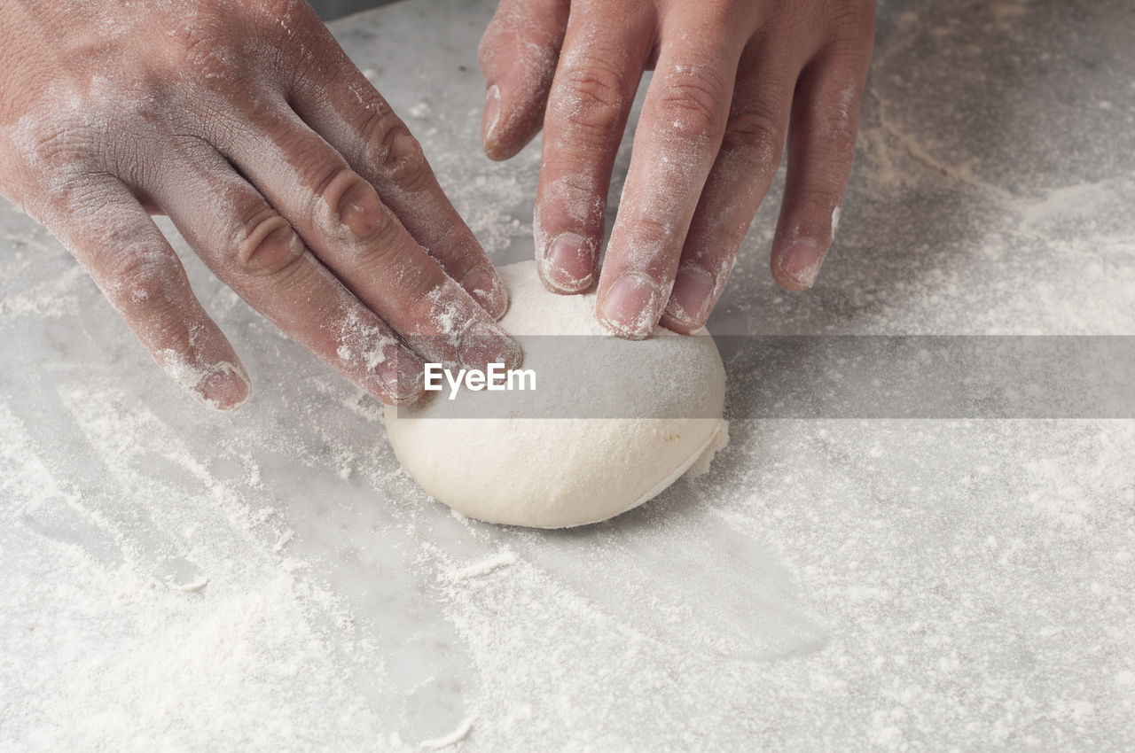 Cropped hands of chef kneading dough on table in commercial kitchen