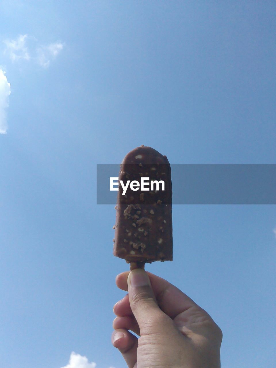 Cropped image of hand holding popsicle against sky