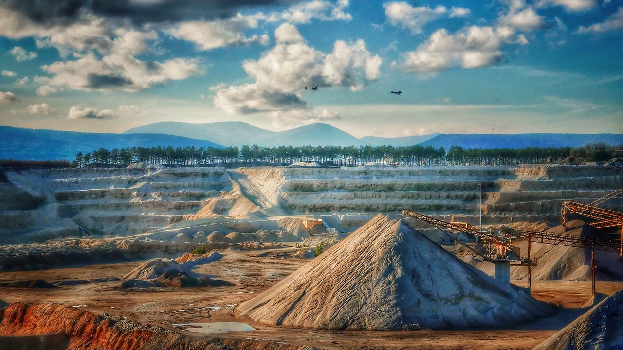 Gravels and cranes against cloudy sky on sunny day