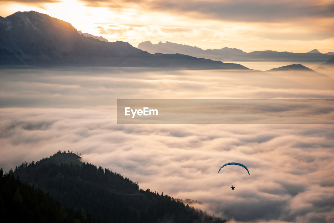 Man paragliding over clouds against cloudy sky during sunset