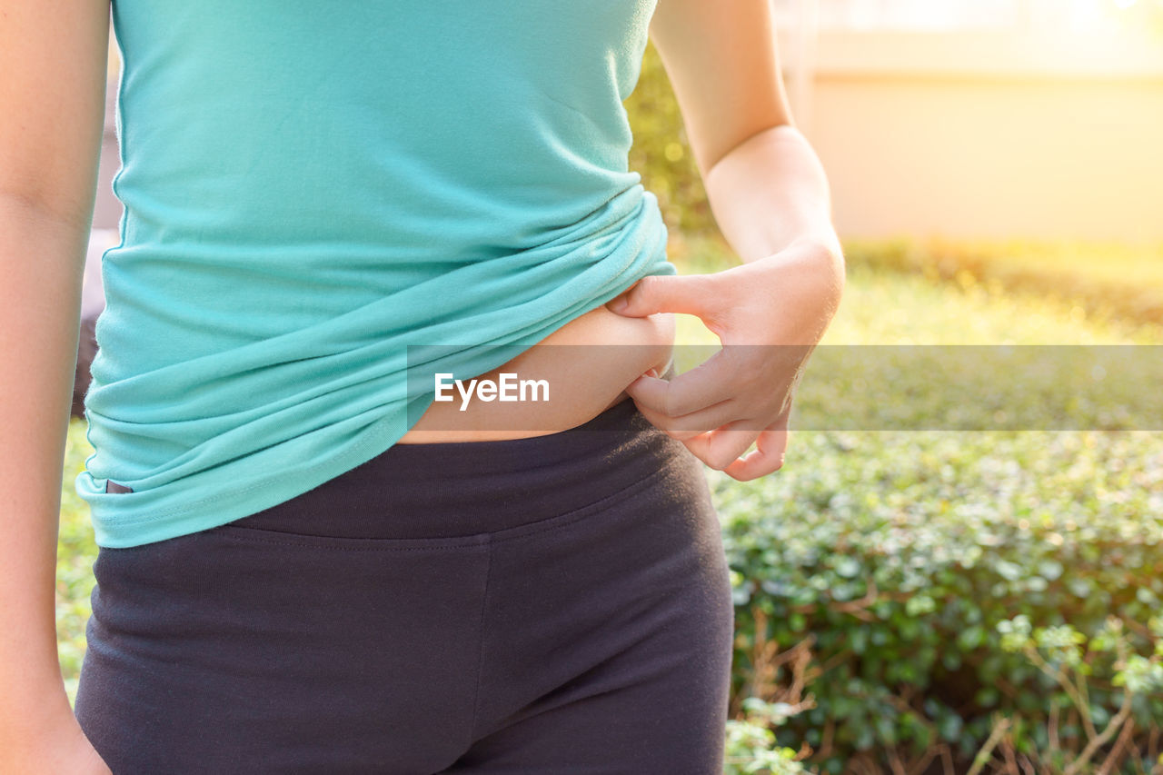 Midsection of woman pinching abdomen while standing outdoors