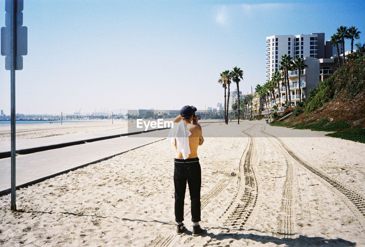 FULL LENGTH REAR VIEW OF MAN STANDING ON CITY STREET