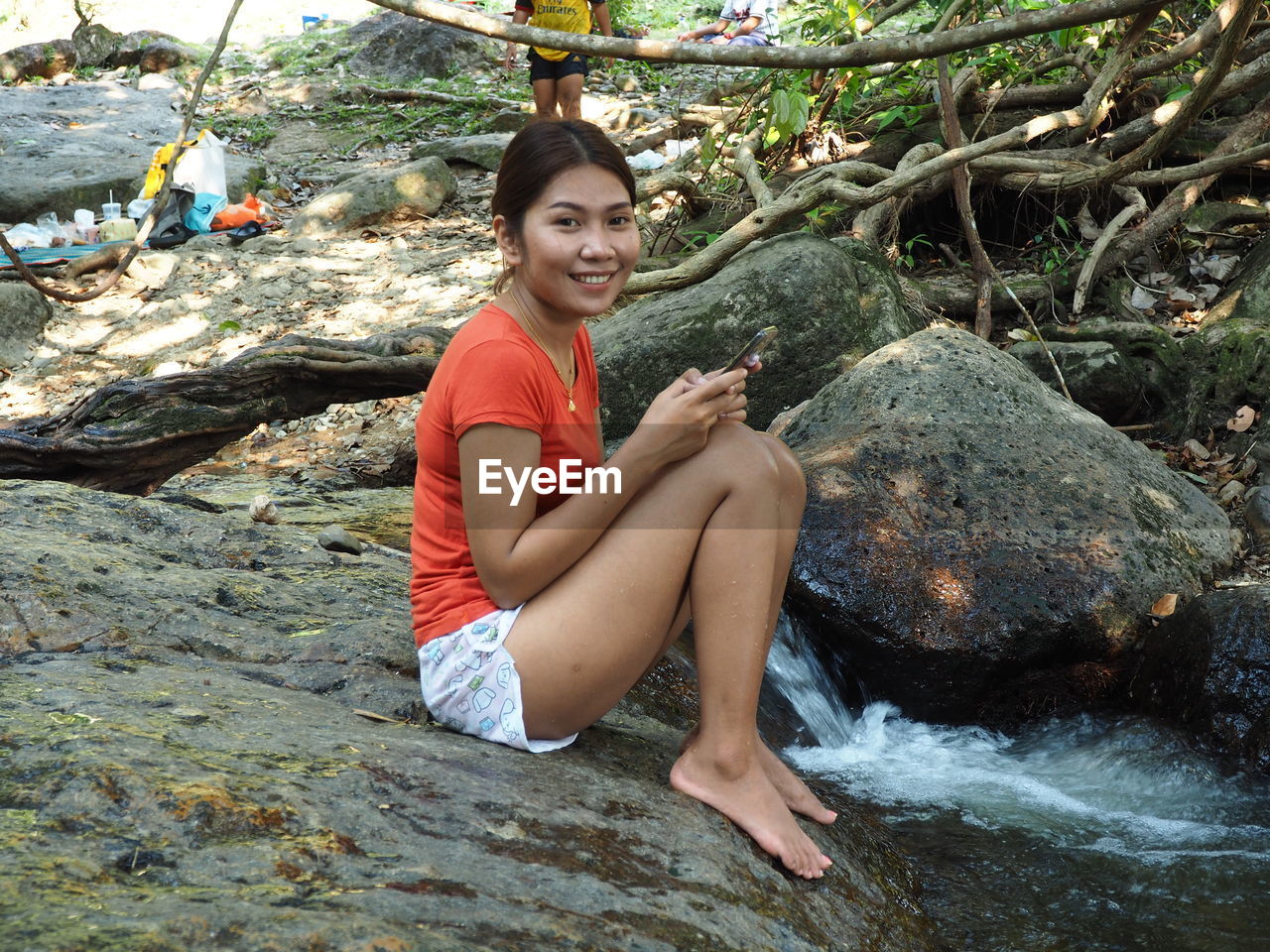 PORTRAIT OF SMILING WOMAN SITTING ON ROCK