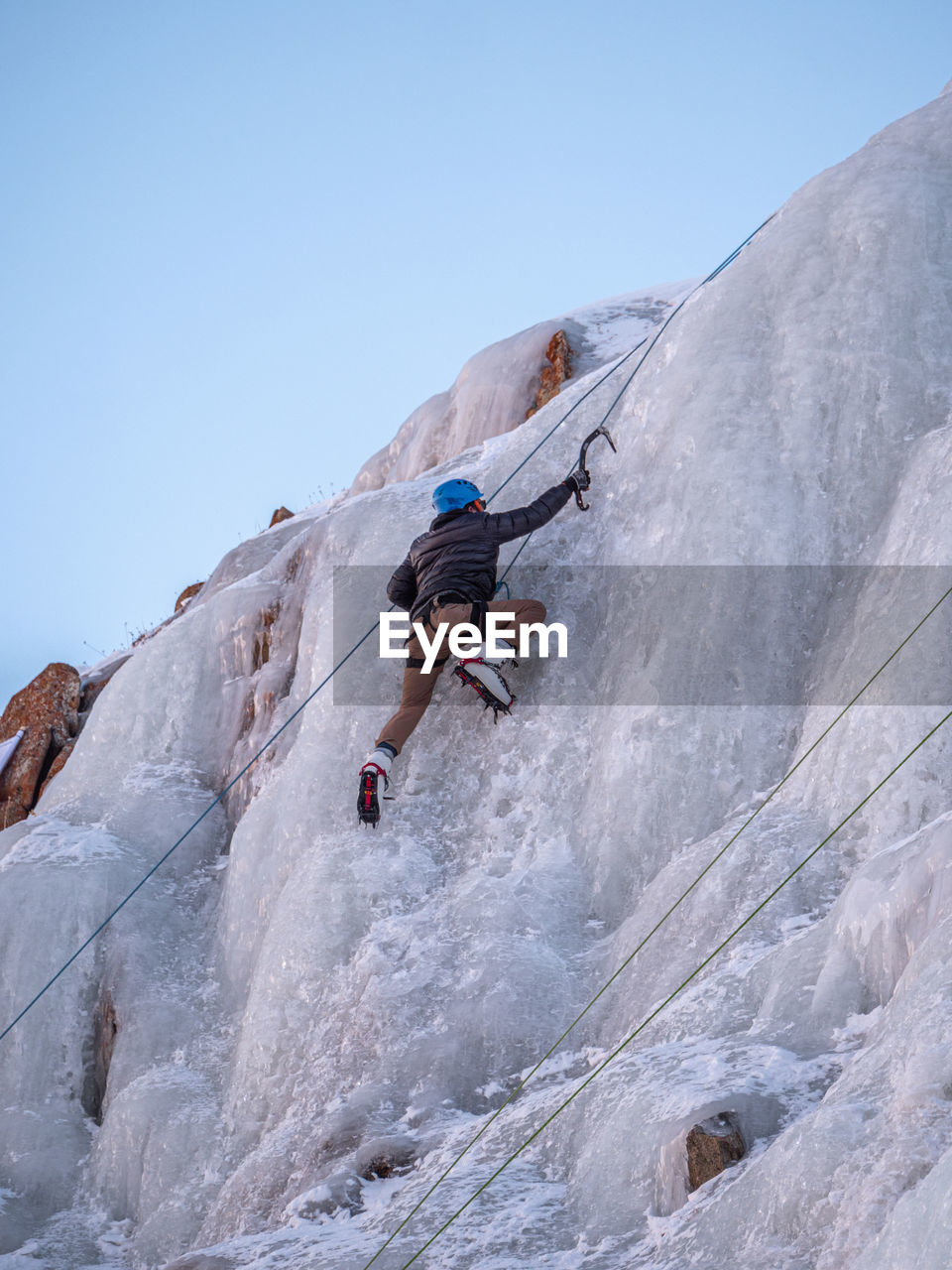 Low angle view of man ice climbing against clear sky