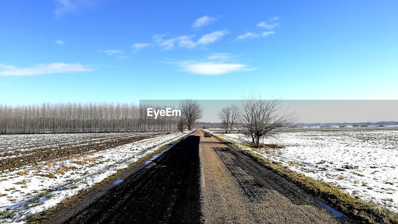 Snow covered road amidst field against sky