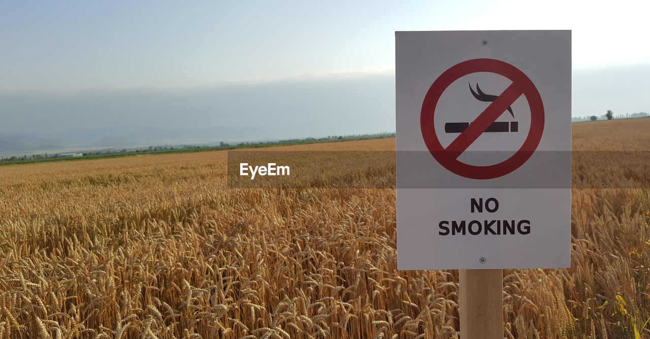 Close-up of information sign on field against sky