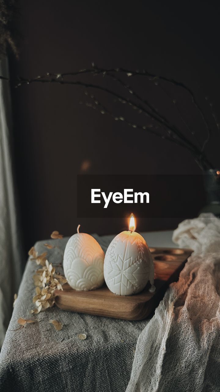 Traditional easter decor.burning soy candles in the shape of white eggs on a brown background