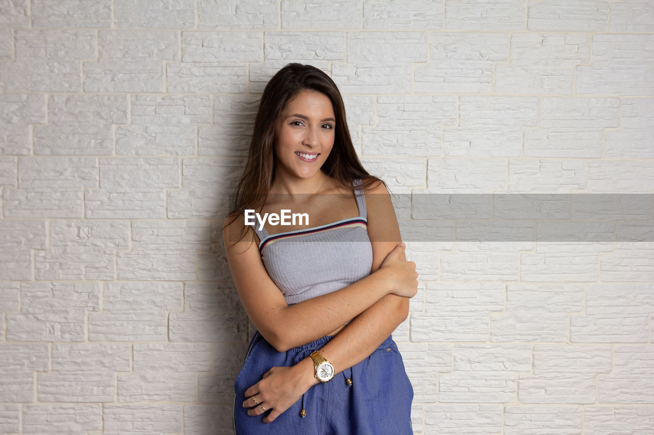 PORTRAIT OF YOUNG WOMAN STANDING AGAINST WALL