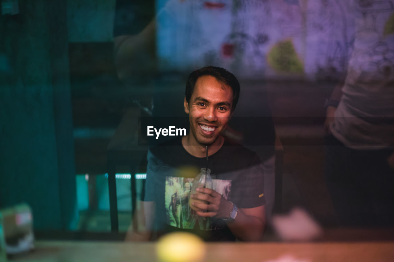 Portrait of young man having drink while sitting at cafe see through window