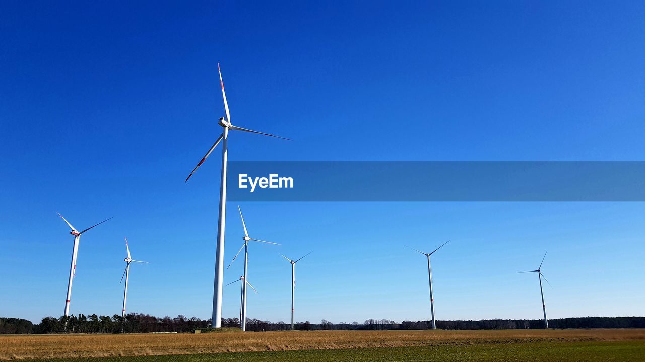 Windmills on field against clear blue sky