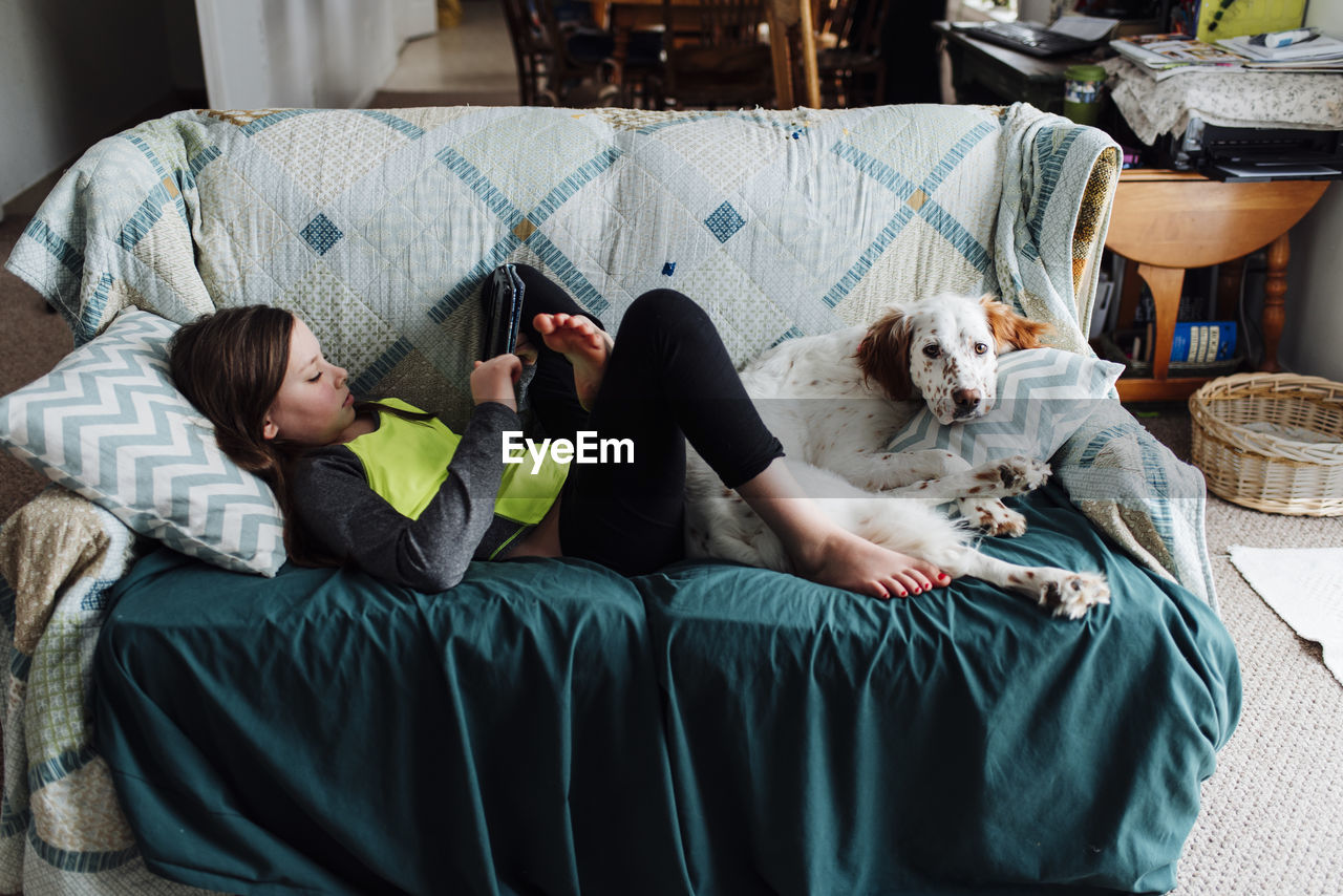 Girl using tablet computer while lying on sofa with dog at home