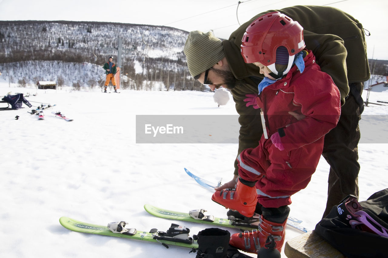 Father helping daughter put on skis