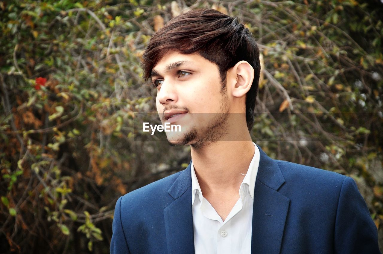 Thoughtful young man wearing suit standing against plants in forest