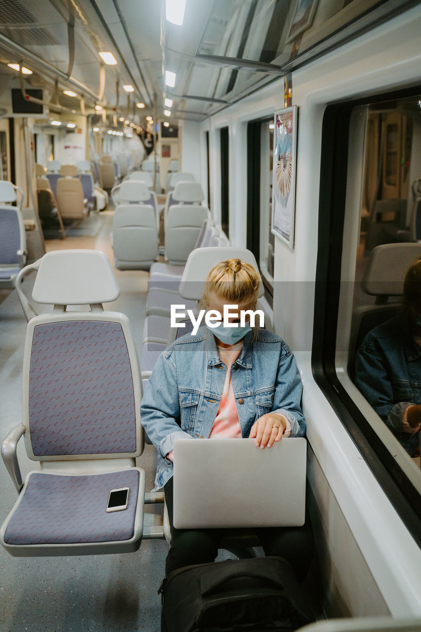 Concentrated female freelancer in medical mask browsing laptop while traveling by train