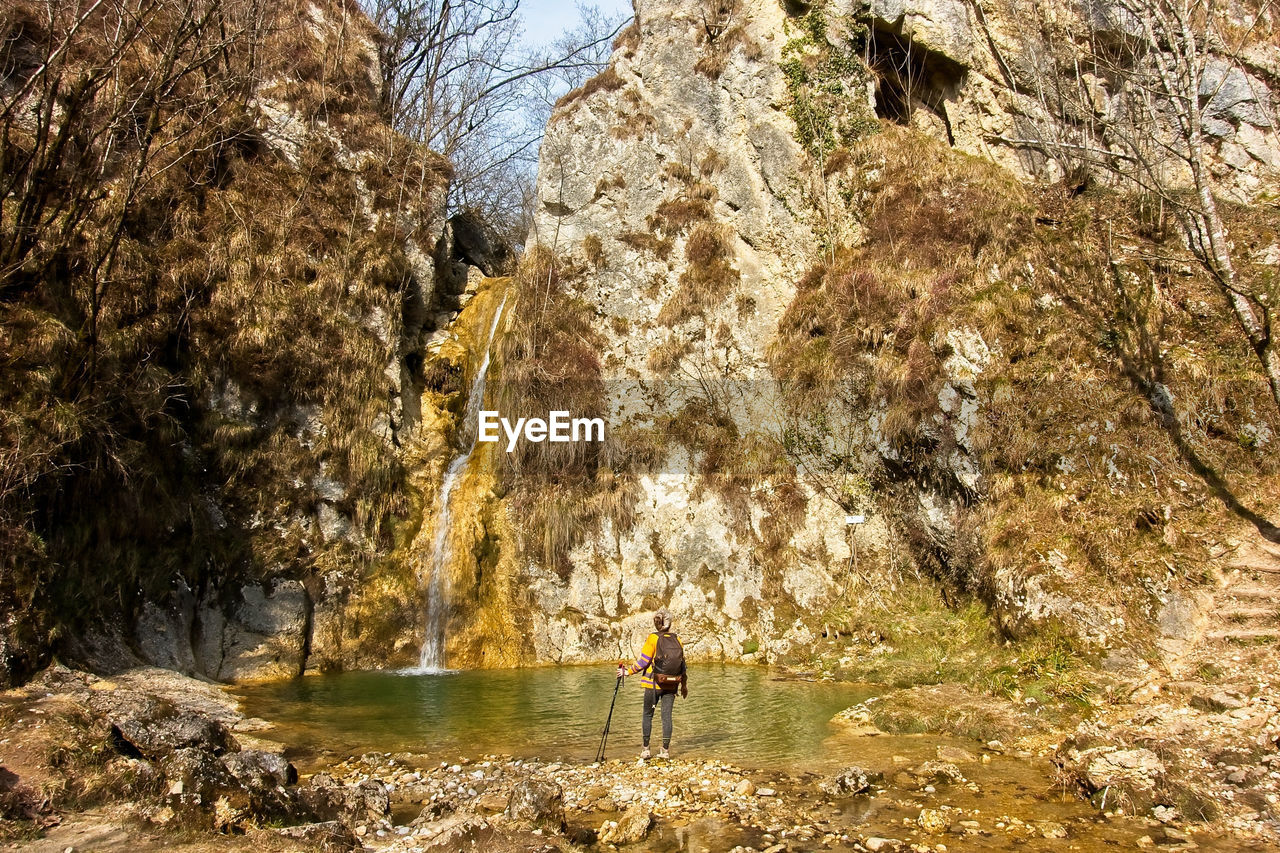 PEOPLE STANDING ON ROCK BY WATER