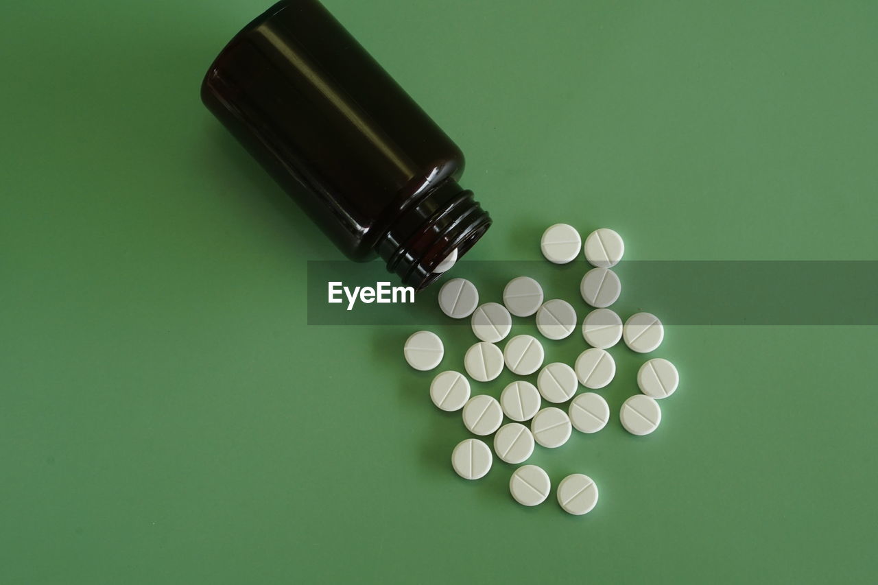 Close-up of pills spilling from bottle against green background