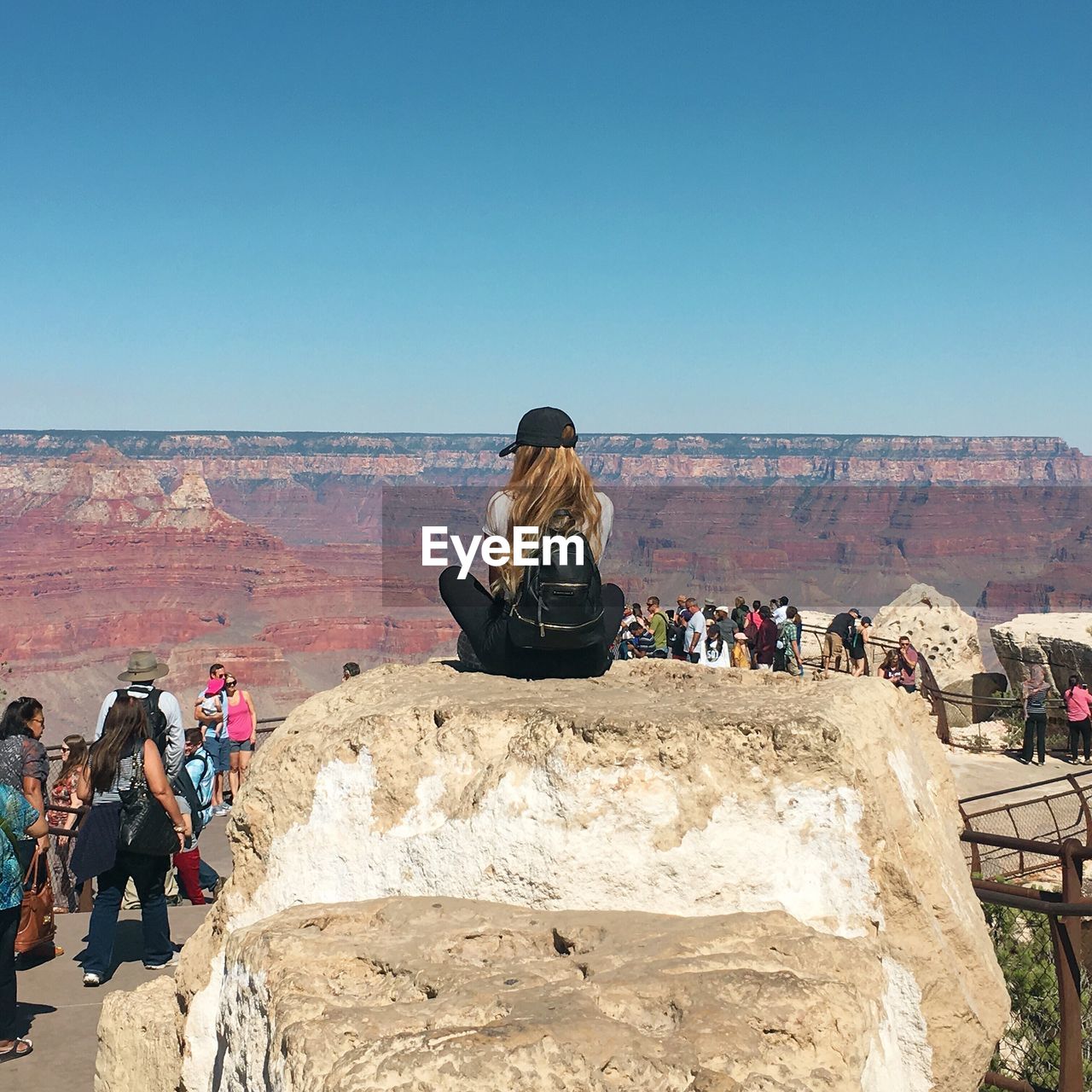 Rear view of woman sitting on rock against sky