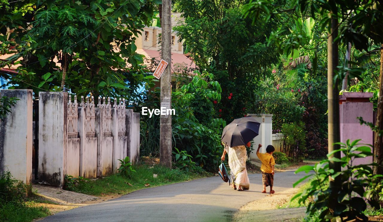 REAR VIEW OF WOMAN WALKING ON ROAD BY TREES