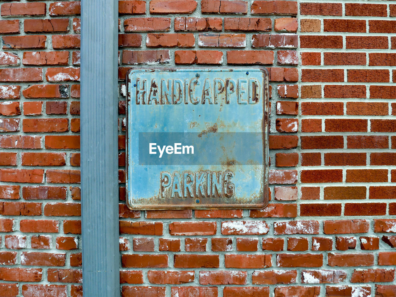 Old metal handicapped parking sign on brick wall