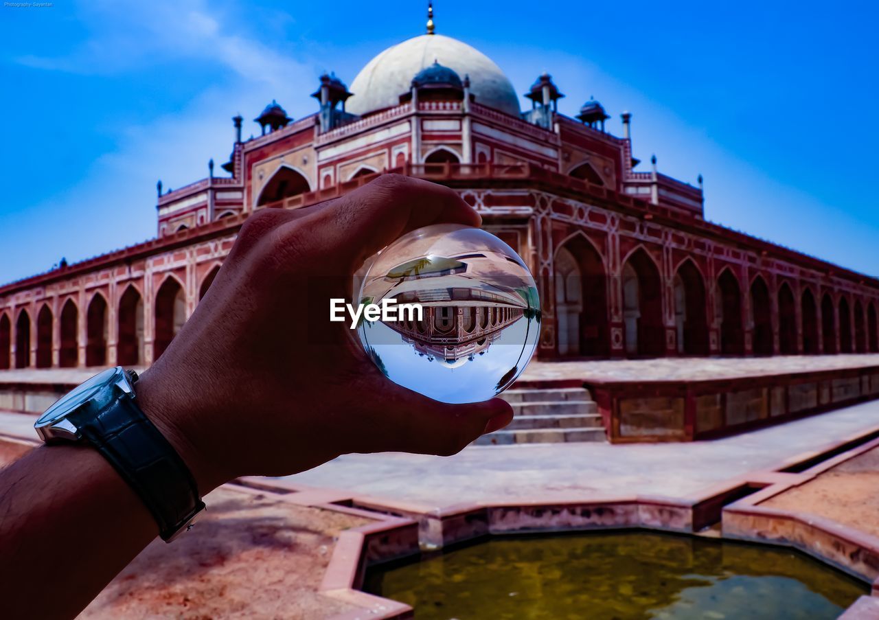 CROPPED IMAGE OF HAND HOLDING HISTORICAL BUILDING