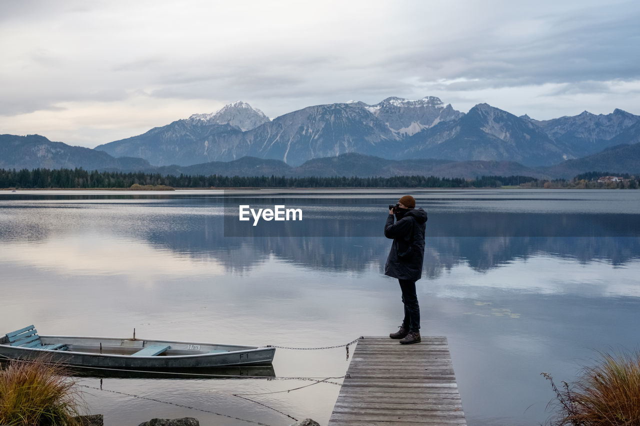 Young man photographing while standing on pier over lake