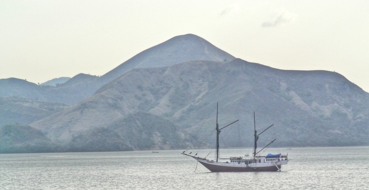 Boat sailing on sea by mountain against clear sky