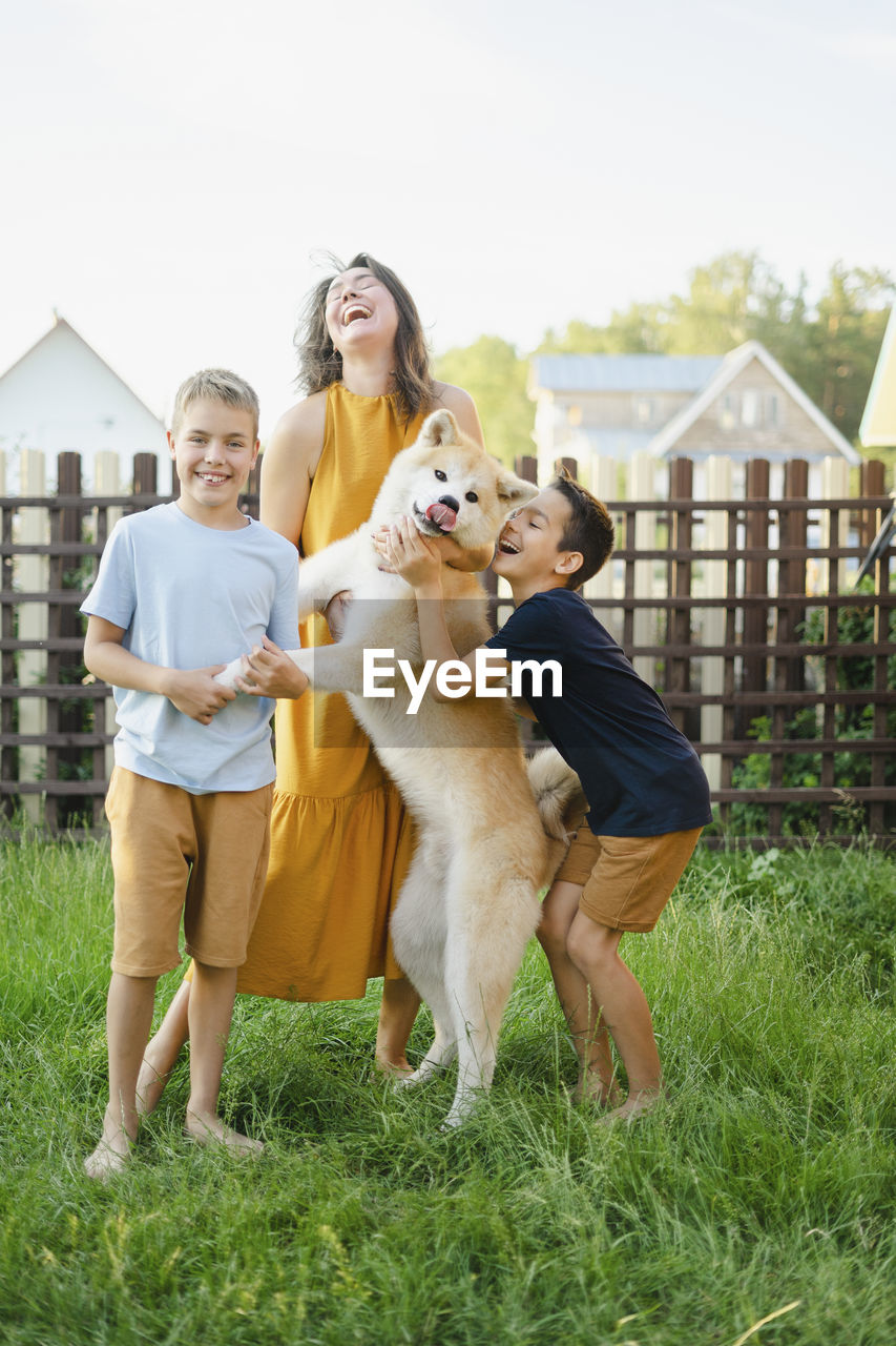 Cheerful family with their akita dog standing on grass in front of fence