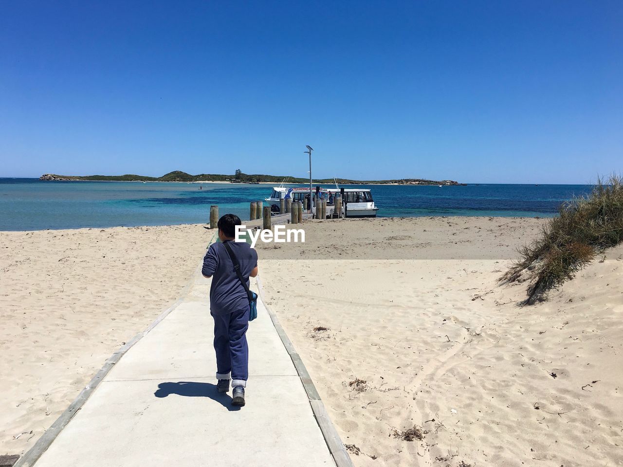 Rear view full length of boy on walkway at beach during sunny day