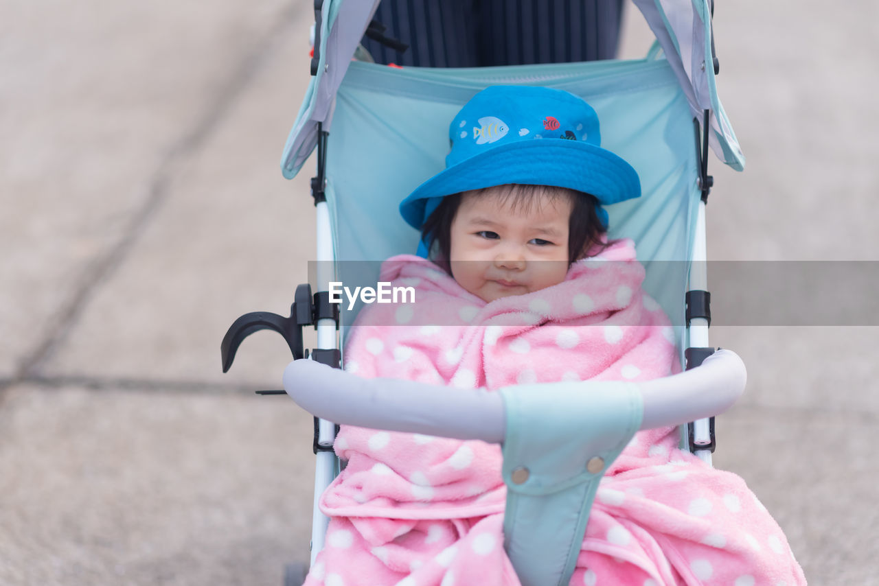 Cute baby wearing hat sitting on baby stroller outdoors