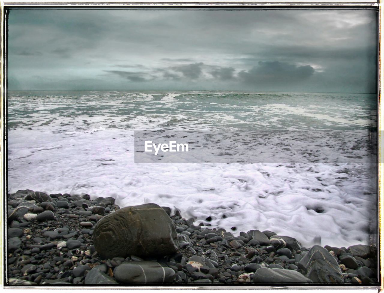 SCENIC VIEW OF SEA AND ROCKS AGAINST CLOUDY SKY