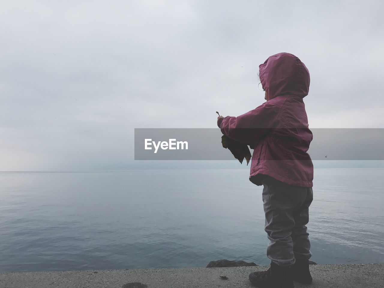 Full length of child standing by lake against cloudy sky during sunset