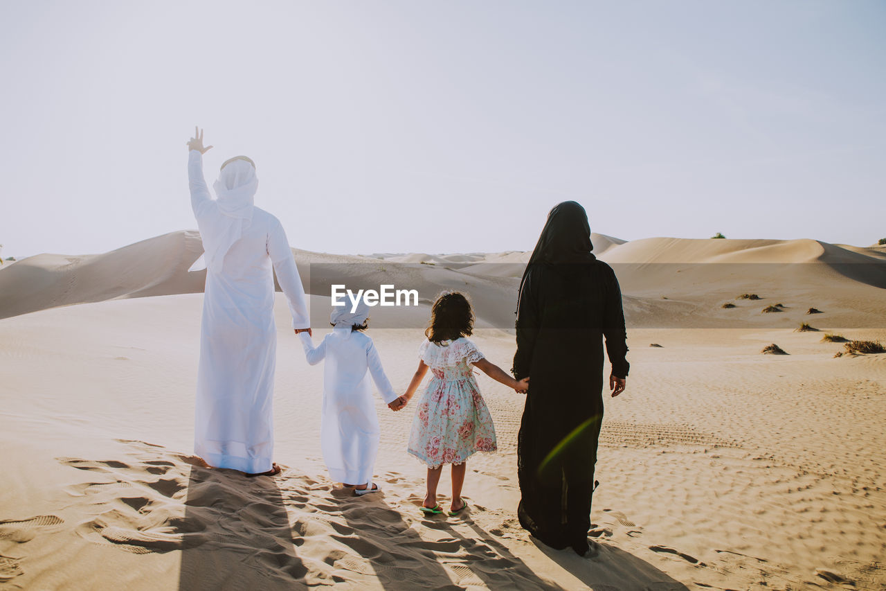 Arabian family standing at desert against sky