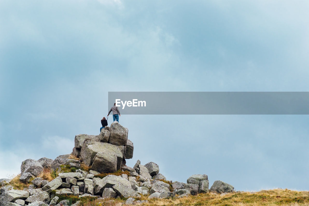 Low angle view of couple on rock formation against cloudy sky