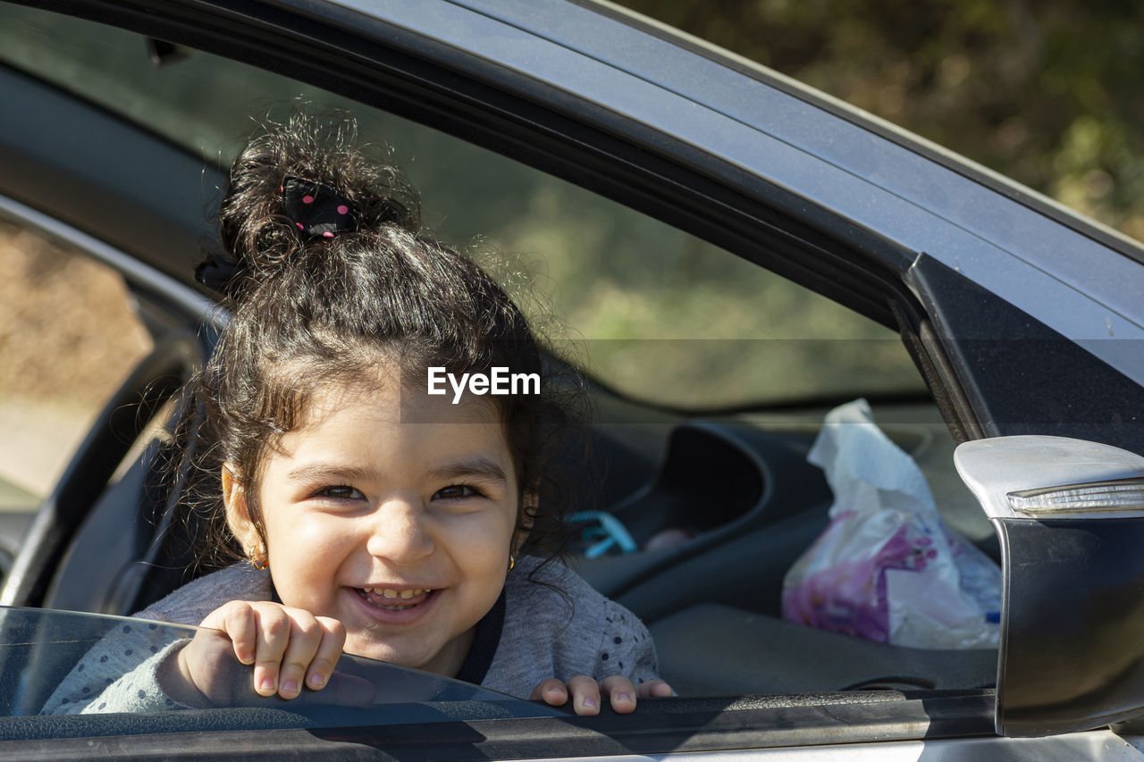 PORTRAIT OF CUTE SMILING GIRL SITTING IN CAR