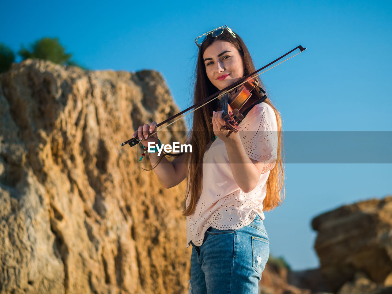 Portrait of young woman playing violin while standing against blue sky