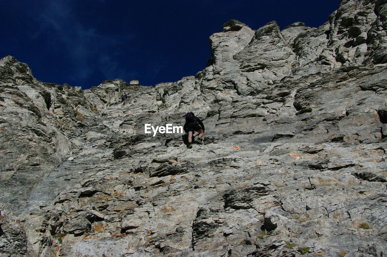 LOW ANGLE VIEW OF MAN ON CLIFF AGAINST MOUNTAIN