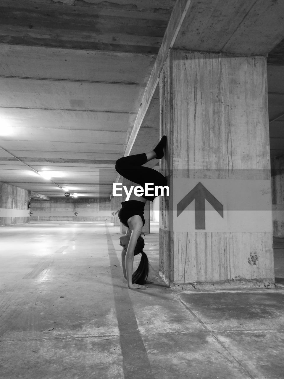 Side view of woman practicing handstand by column at illuminated parking garage