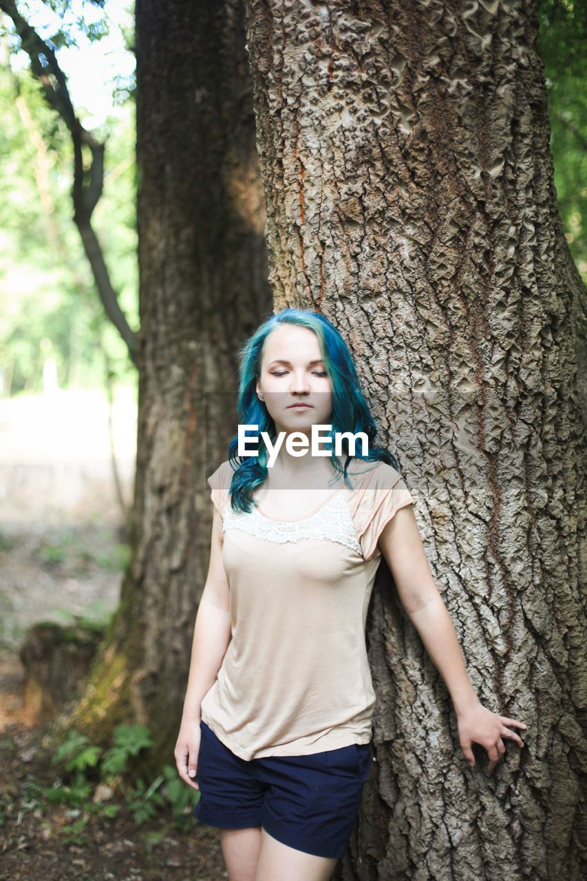 Young woman standing by tree trunk at park