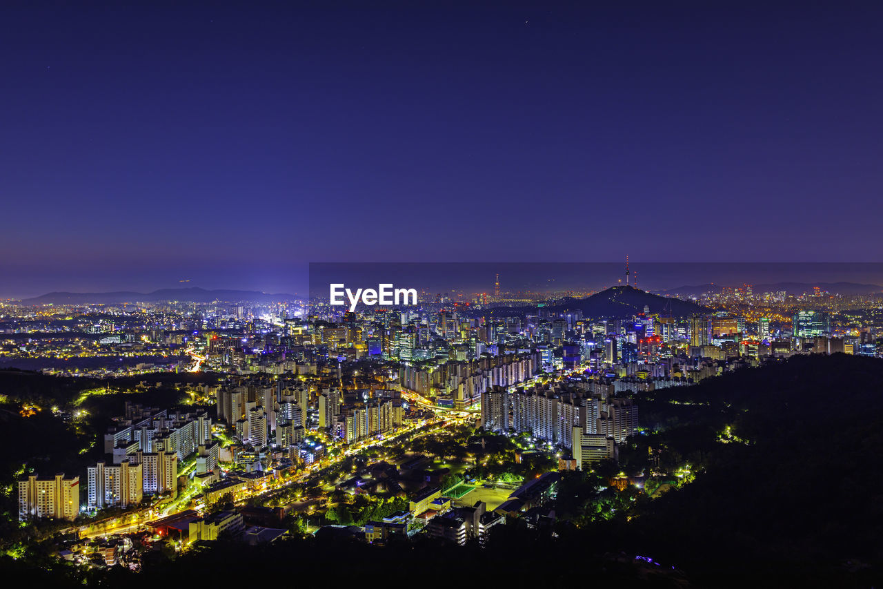 HIGH ANGLE VIEW OF ILLUMINATED CITY AGAINST CLEAR BLUE SKY