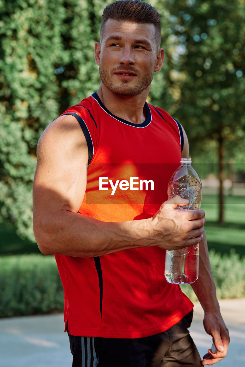 portrait of young man lifting dumbbell while standing outdoors