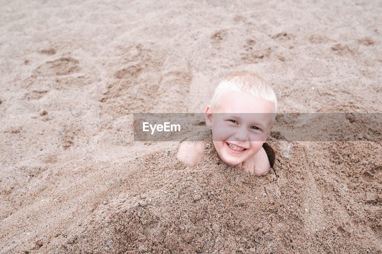 Portrait of smiling boy buried in sand at beach