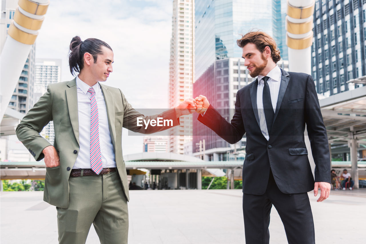 Businessmen bumping fist while standing against building in city