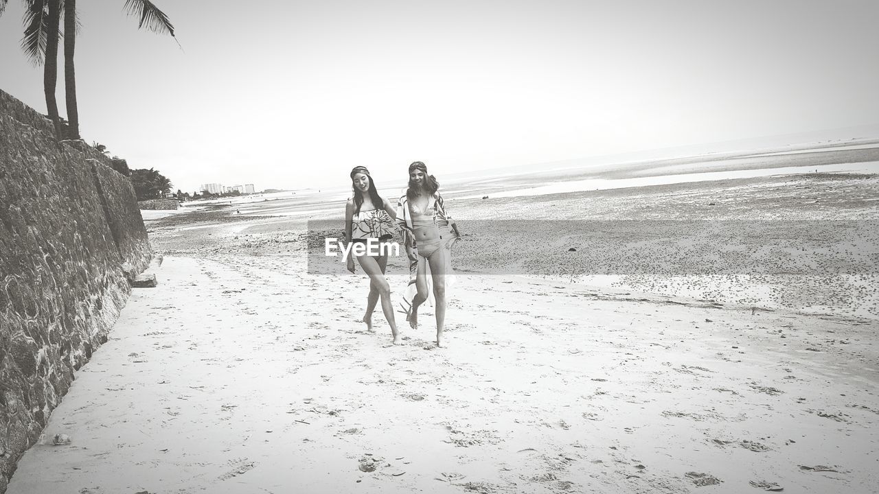 Full length of female friends walking at sandy beach