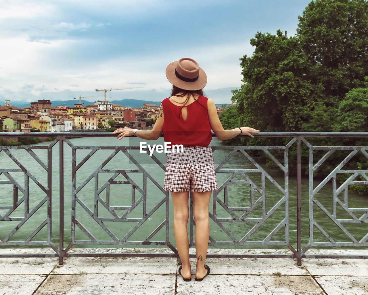 Full length of young woman standing by railing on bridge over river against sky