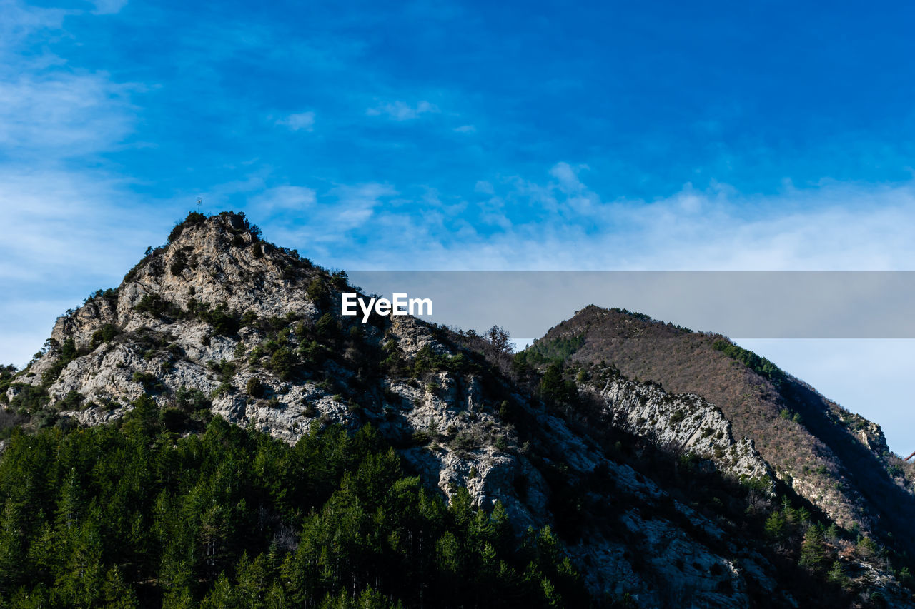 Low angle view of rocks on mountain against blue sky