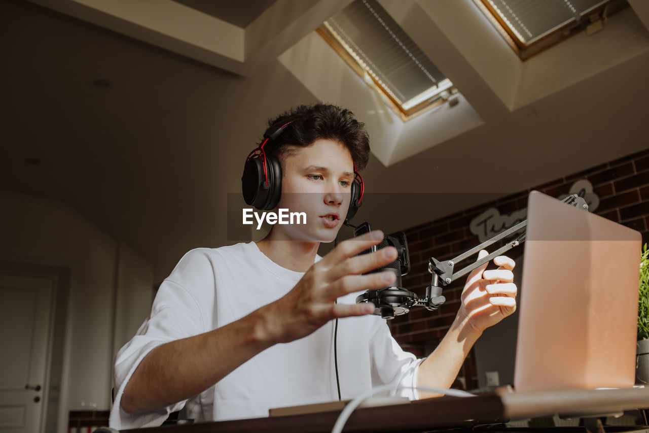 Teenage boy podcasting in front of laptop at home