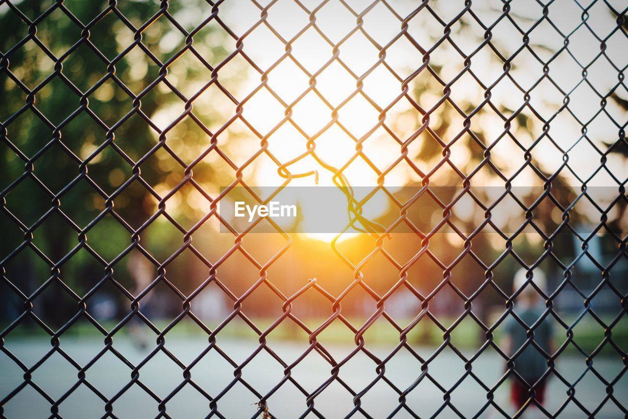 Damaged chainlink fence against sky during sunny day