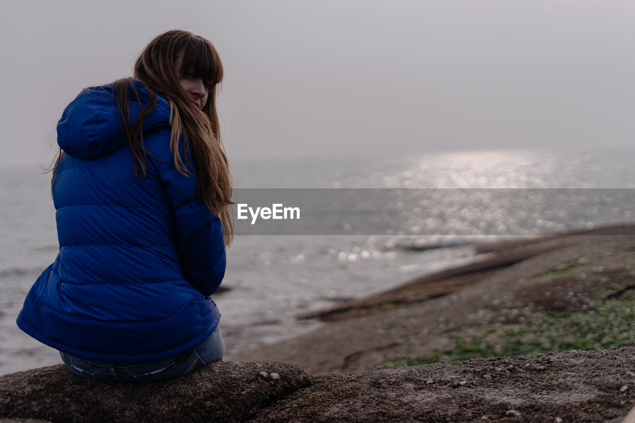 Rear view of woman sitting on rock formation against sea